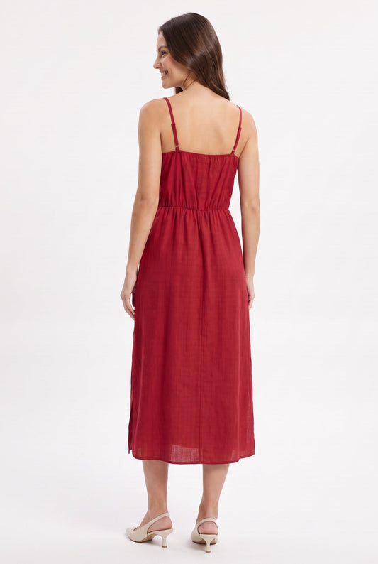 A woman modeling a red midi dress from the back, showing the thin spaghetti straps, gathered waist, and flowing skirt, set against a plain white studio background.
