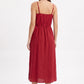 A woman modeling a red midi dress from the back, showing the thin spaghetti straps, gathered waist, and flowing skirt, set against a plain white studio background.
