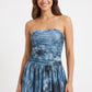 A woman modeling a strapless blue mini dress with a tie-dye pattern, standing against a plain white studio background.